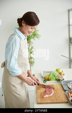 Frau in Schürze, die Fleisch grillt Stockfoto