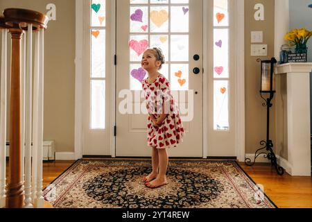 Ein lächelndes Mädchen im Kleid mit Herzmuster steht an verzierten Glastüren Stockfoto