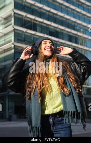 Glückliche junge Frau, die Musik mit Kopfhörern in der Stadt hört Stockfoto