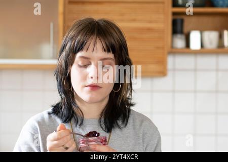 Eine junge Frau isst Marmelade in der Küche Stockfoto