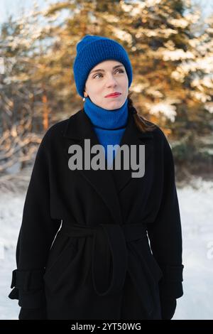 Junge Erwachsene Frau, die im Winterwald wegschaut Stockfoto