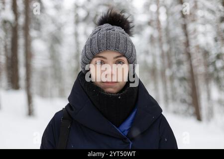Junge Erwachsene hübsche Frau, die im Winterwald in die Kamera schaut Stockfoto