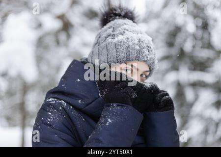 Frau, die ihr Gesicht in einem klobigen Schal im schneebedeckten Wald versteckt Stockfoto