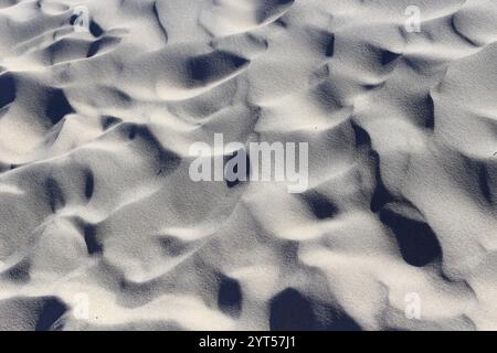 Eine Nahaufnahme der Sandstruktur an einem Strand, die die komplizierten Muster von Licht und Schatten zeigt. Das Spiel des Sonnenlichts hebt den subtilen Kamm hervor Stockfoto