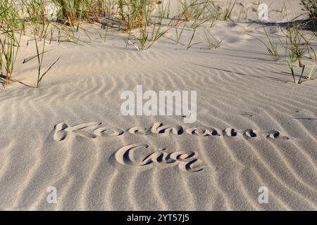 Eine romantische Botschaft von „Kocham Cię“ (ich liebe Sie auf Polnisch), geschrieben im Sand an einem wunderschönen Strand, mit den Wellen des Ozeans sanft im Hintergrund. Stockfoto