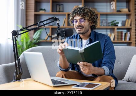 Ein Mann mit Brille nimmt einen Podcast von zu Hause auf, indem er ein Mikrofon, einen Laptop und ein Telefon benutzt. Er bezieht sich während des Sprechens auf Notizen in einem Buch und erstellt ansprechende Inhalte für sein Publikum. Stockfoto