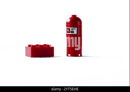 Ein roter Lego-Stein befindet sich neben einem roten Hydranten. Der Hydrant ist rot und mit einem weißen Etikett versehen. Lego. Polen, Warschau 06.12.2024 Stockfoto