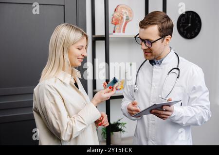 Männlicher Arzt, der einen Aerosolinhalator in der Hand hält, bei einer Demonstration einer Patientin in seiner Praxis. Stockfoto