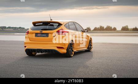 Dottergelb Ford Focus ST auf einer Rennstrecke. Drei Viertel Rückansicht des Fließhecks, der auf einer riesigen Asphaltfläche geparkt ist. Stockfoto