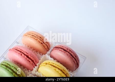 Französische Macarons mit weißer Paperpan in transparenter Plastikverpackung auf grauem Hintergrund, bunte Kuchen mit verschiedenen Geschmacksrichtungen. Appetitliches Dessert, Stockfoto