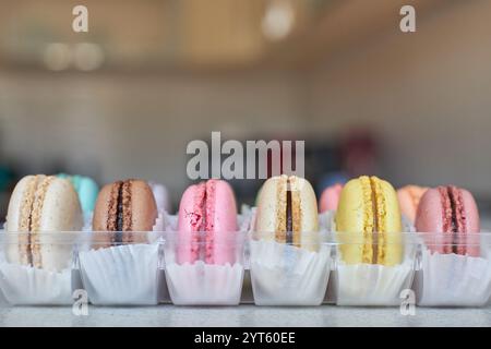 Französische Macarons mit weißer Paperpan in transparenter Plastikverpackung in der Küche, bunte Kuchen mit verschiedenen Geschmacksrichtungen. Appetitliches Dessert, Makronen Stockfoto