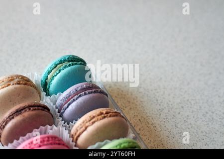 Helle französische Macarons mit weißer Paperpan in transparenter Plastikverpackung, grauer Hintergrund, bunte Kuchen verschiedene Geschmacksrichtungen. Appetitliches Dessert, Stockfoto