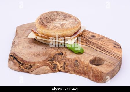 Englischer Muffin mit Räucherschinken und schweizer Käse auf einem Olivenholzbrett Stockfoto