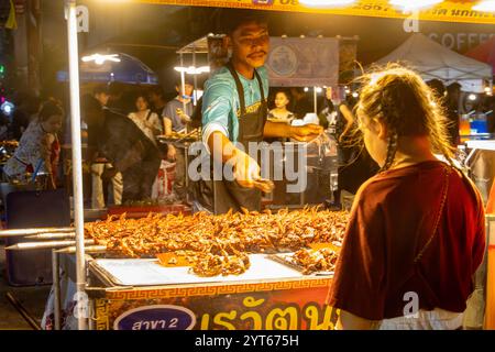 SAMUT PRAKAN, THAILAND, 26. Oktober 2024, Ein Mädchen wählt gegrillte Wachteln an einem Nachtmarkt-Kiosk Stockfoto