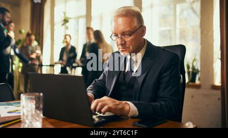 Konzentrierter Geschäftsmann, der während eines professionellen Networking-Events auf dem Laptop schreibt und dabei Engagement und Effizienz demonstriert. Stockfoto