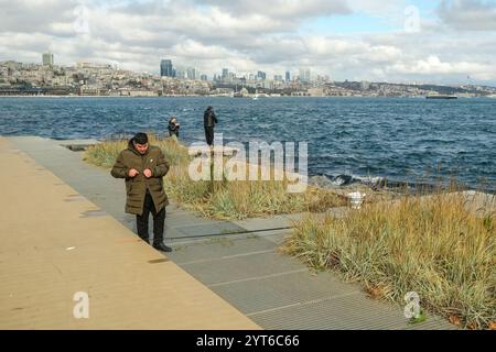 Ein Mann, der seine Angelausrüstung vorbereitet, während andere im Hintergrund fischen. Amateurfischer wurden am Bosporus mit Angelruten gefischt. Stockfoto