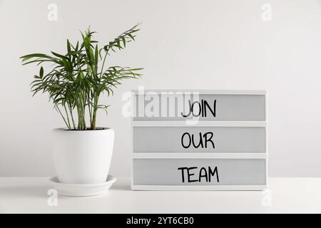 Brieftafel mit Text, begleiten Sie unser Team und die Zimmerpflanze auf dem weißen Tisch. Personalabteilung Stockfoto