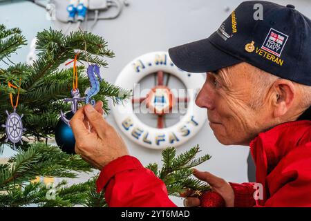 London, Großbritannien. Dezember 2024. Der Baum wird auf dem Vierteldeck von Freiwilligen dekoriert, darunter Johnny Banks - We Were There Veteran (ex Royal Marine) - die aktuelle Crew und die Freiwilligen an Bord der HMS Belfast beginnen eine neue jährliche festliche Tradition, einen Weihnachtsbaum vom Borough Market zurückzubringen, um das Vierteldeck im Geiste zu dekorieren, wie die Besatzung der HMS Belfast 1943 Weihnachten während der arktischen Konvois gefeiert hätte. Guy Bell/Alamy Live News Stockfoto