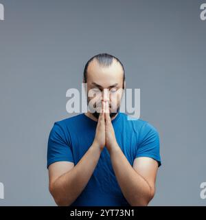 Ein besinnlicher Mann mit gefalteten Händen reflektiert in einem Moment der Selbstbetrachtung, sein heiterer Ausdruck vermittelt ein Gefühl von Frieden und Achtsamkeit gegen A Stockfoto