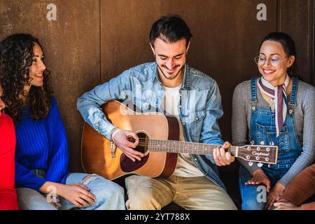 Junger Musiker, der Akustikgitarre spielt und seine Freunde unterhält Stockfoto
