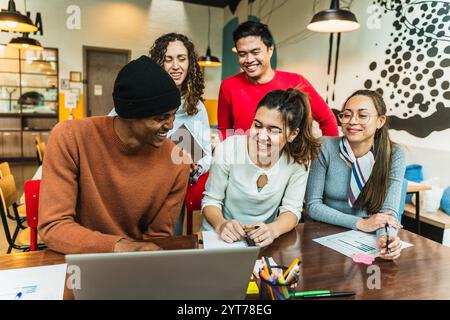 Ein vielfältiges Team von Kollegen arbeitet an einem Projekt zusammen, nutzt einen Laptop und teilt Ideen in einer modernen Büroumgebung Stockfoto