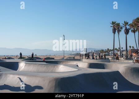 Der Skatepark Venice Beach verfügt über glatte Betonrampen und -Schüsseln. Skater und Zuschauer genießen die Szene mit Palmen, Sandstrand und fernen mou Stockfoto