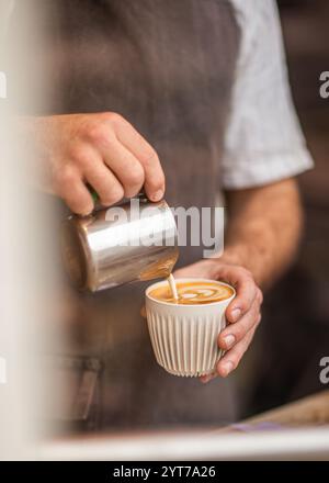 Nahaufnahme eines Barista, der aufgeschäumte Milch in eine Tasse gießt, um Latte Art zu kreieren. Stockfoto