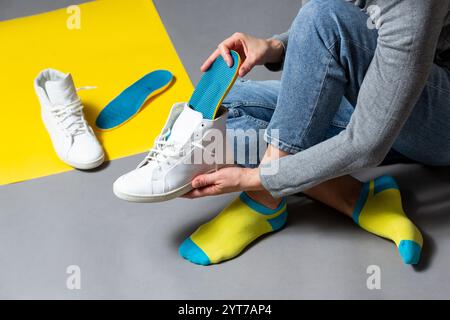 Nahaufnahme von weiblichen Händen, die orthopädische Einlegesohlen in weiße Turnschuhe stecken. Medizinische und orthopädische Behandlung und Prävention von Plattfüßen Konzept. Stockfoto