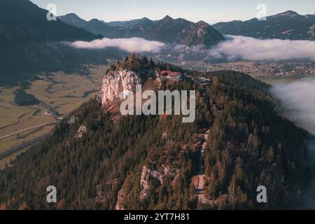 Die Ruine der Burg Falkenstein bei Pfronten im Allgäu. Umgeben von Wald steht die Burg auf einem Hügel, während Nebel im Tal liegt. Die Berge des Alpenvorlandes im Hintergrund. Stockfoto