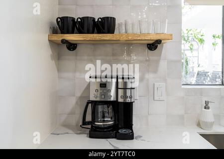 Kombination aus Kaffeemaschine und ein-Tassen-Brühmaschine auf einer weißen Küchenarbeitsfläche mit Tassen, Tassen und Gläsern auf einem Regal. Stockfoto