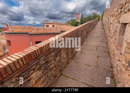 Steinweg entlang der historischen Stadtmauern von Girona, Spanien, mit Blick auf Terrakotta-Dächer und einen weit entfernten Glockenturm unter einer dramatischen Wolke Stockfoto