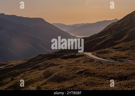 Blick von der Crowns Range auf der Südinsel Neuseelands in Richtung Queenstown. Die Sonne untergeht gerade und taucht die Landschaft in goldenes Licht. Stockfoto