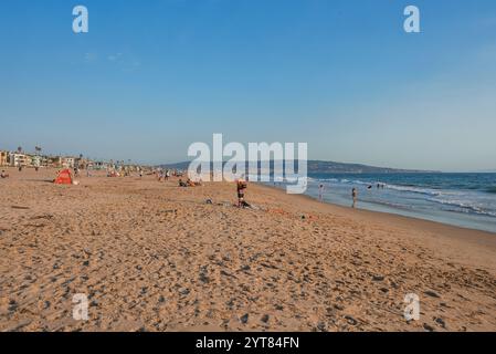 Venice Beach in Los Angeles bietet Menschen am Sandstrand, Gebäude am Strand und eine ferne hügelige Landschaft unter klarem blauen Himmel. Stockfoto