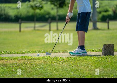 Ein junger Mann in schicker Sportkleidung spielt an sonnigen Tagen im Freien Golf. Der Mann ist dabei, den Golfball mit einem Profi-Schläger zu schlagen. Stockfoto
