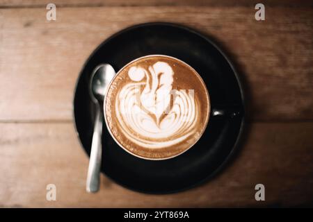 Künstlerischer Latte mit Schaumstoffdesign, serviert in einer schwarzen Tasse auf dem Tisch Stockfoto