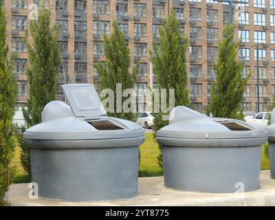 Zwei offene unterirdische Mülllagertanks in einem Innenhof vor dem Hintergrund von Wohngebäuden und Autos auf dem Parkplatz Stockfoto