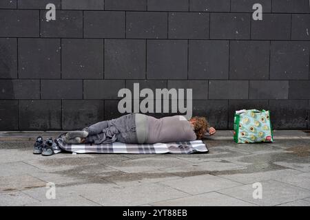 Deutschland, Nordrhein-Westfalen, Köln, junger Obdachloser, der draußen auf einem gepflasterten Boden schläft Stockfoto