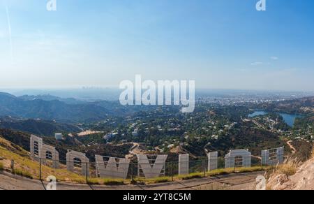 Das Bild fängt das Hollywood-Schild von hinten ein und zeigt die Stadtlandschaft von Los Angeles, die sanften Hügel und ein Reservoir unter einem klaren blauen Himmel. Stockfoto