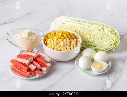 Zutaten für Salat: Süßmais aus der Dose, Surimi-Sticks, frischer napa-Kohl, gekochte Eier und Mayo auf Marmorarbeitsfläche. Mamas Salatrezept. Stockfoto