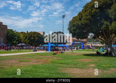 Eine große Menschenmenge versammelt sich um Zelte auf dem grasbewachsenen Feld der UCLA, eingerahmt von Bäumen und einem klaren Himmel. Ein blauer Torbogen und ein Lichtmast sind im Hintergrund sichtbar Stockfoto