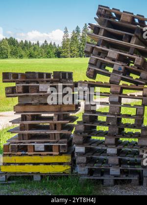 Landschaftsansicht mit leeren, unordentlich gestapelten Paletten im Vordergrund auf einer grünen Weide im Sommer Bayerns. Stockfoto