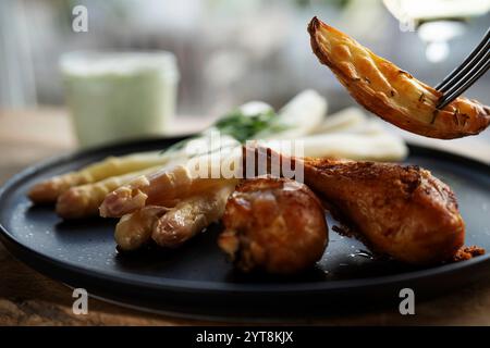 Gebratene Hähnchenschenkel mit Spargel und gegrillten Kartoffeln auf einer schwarzen Keramikplatte. Stockfoto