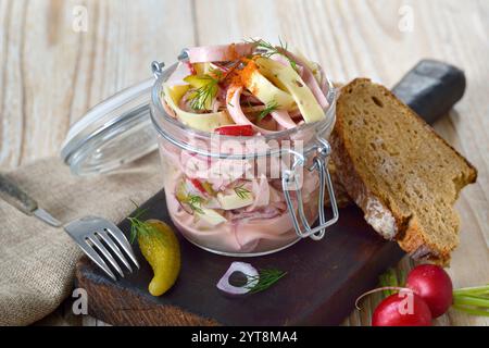 Herzhafter Schweizer Wurstsalat mit Käsestreifen und eingelegten Gurken in einem Glas, serviert mit rustikalem Bauernbrot Stockfoto