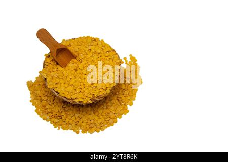 Eine Korbschale gefüllt mit gelben Linsen, mit einem Holzlöffel und umgeben von verstreuten gelben Linsenkörnern. Stockfoto