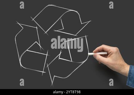 Männliche Hand mit weißem Buntstift bemalt Recycling-Symbol über dunklem Brett Stockfoto