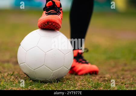 Ansicht der Beine einer brünetten Fußballspielerin, die zum Kicken des Fußballs läuft. Auf einem grünen Gras draußen, mit farbenfrohem Hintergrund. Mit Sportbekleidung. Stockfoto