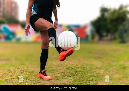 Ansicht der Beine einer brünetten Fußballspielerin, die zum Kicken des Fußballs läuft. Auf einem grünen Gras draußen, mit farbenfrohem Hintergrund. Mit Sportbekleidung. Stockfoto