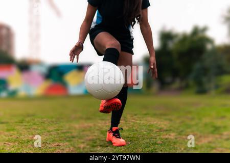 Ansicht der Beine einer brünetten Fußballspielerin, die zum Kicken des Fußballs läuft. Auf einem grünen Gras draußen, mit farbenfrohem Hintergrund. Mit Sportbekleidung. Stockfoto