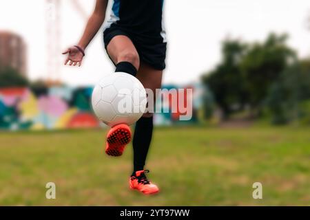 Ansicht der Beine einer brünetten Fußballspielerin, die zum Kicken des Fußballs läuft. Auf einem grünen Gras draußen, mit farbenfrohem Hintergrund. Mit Sportbekleidung. Stockfoto