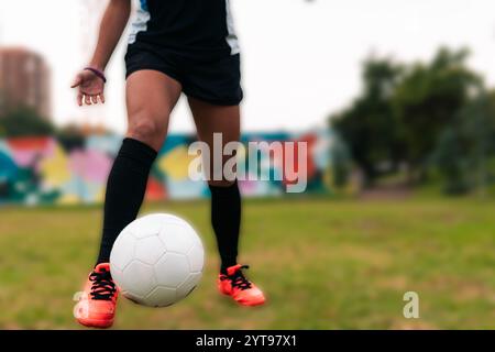 Ansicht der Beine einer brünetten Fußballspielerin, die zum Kicken des Fußballs läuft. Auf einem grünen Gras draußen, mit farbenfrohem Hintergrund. Mit Sportbekleidung. Stockfoto